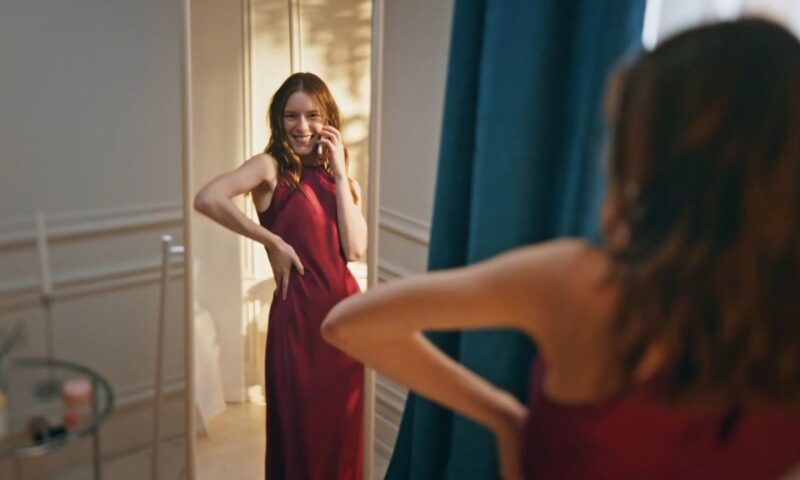 devojka se gleda u ogledalo i pozira u dugoj bordo haljini bez rukava