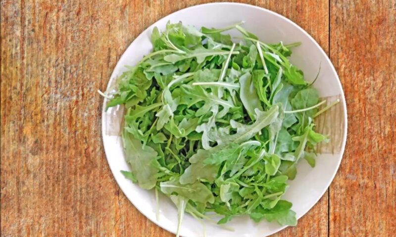 rukola u beloj činiji na drvenom stolu