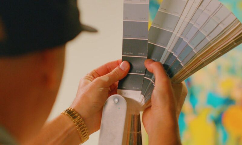 čovek drži u rukama paletu boja i bira sa kojom će okrečiti zid